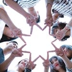 A circle of friends forming a star shape with fingers, symbolizing unity and teamwork.