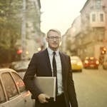 Businessman in a suit holding a laptop on a busy city street. Urban professional life.
